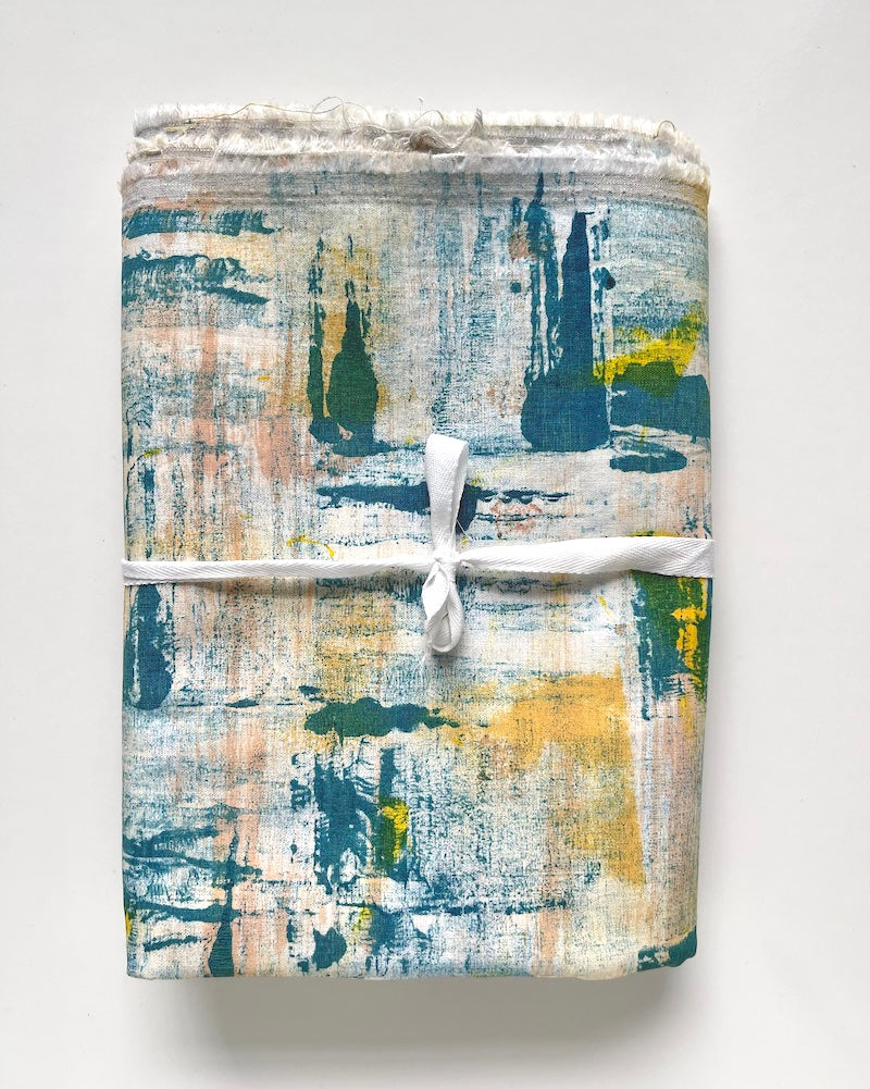 One piece of hand-painted fabric featuring shades of blue, yellow, orange and tan paint arranged in an abstract design. The fabric is folded and tie with a white ribbon.